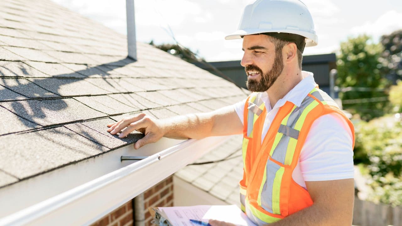 A roofer in a hard hat inspecting shingles