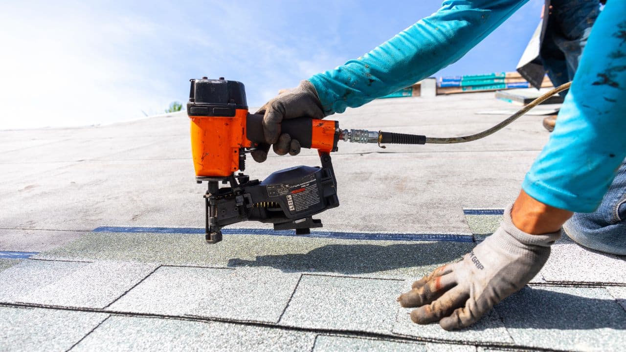 A roofer fastening shingles with a nail gun