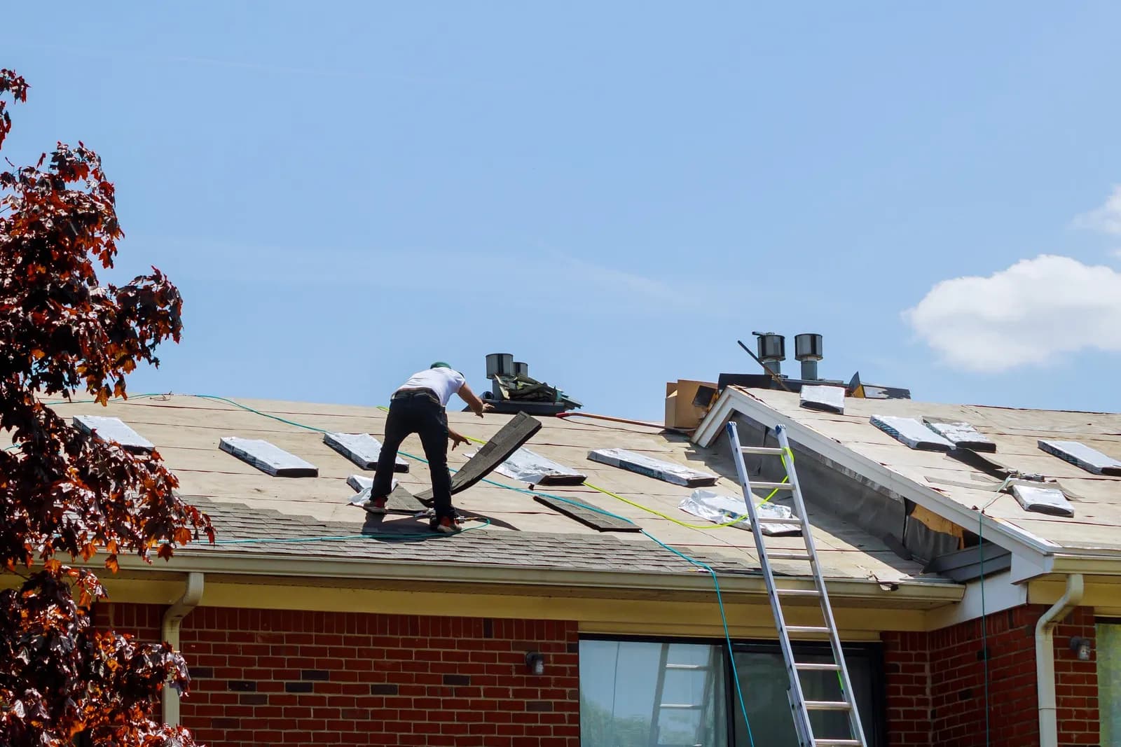 Roofers working on a brick ranch home, ladder against the eaves
