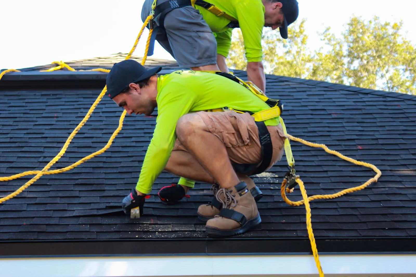 Two roofers on safety lines on a shingle roof